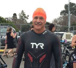 Man in wetsuit and swim cap is ready to start Carpinteria triathlon.